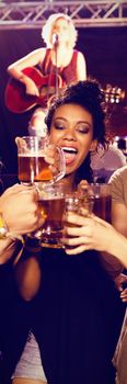 Smiling friends toasting beer glasses with performer singing in background at nightclub