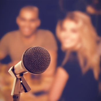 Microphone with stand against smiling young friends sitting at nightclub