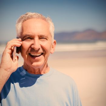 Portrait of senior man talking on mobile phone at beach during sunny day