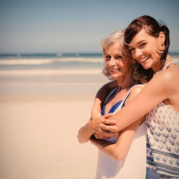 Portrait of happy woman embracing her mother at beach during sunny day