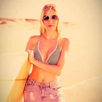 Portrait of young woman holding surfboard at beach during sunny day