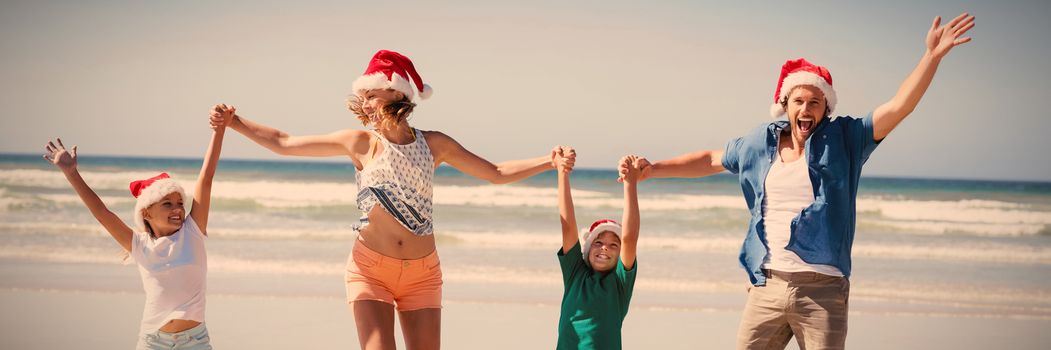 Cheerful family wearing Santa hat while jumping on shore at beach during sunny day
