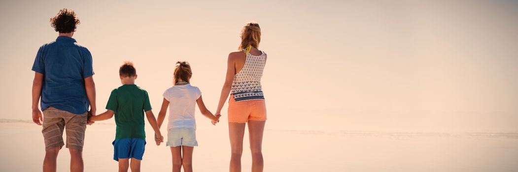 Rear view of family holding hands while standing together on shore at beach during sunny day