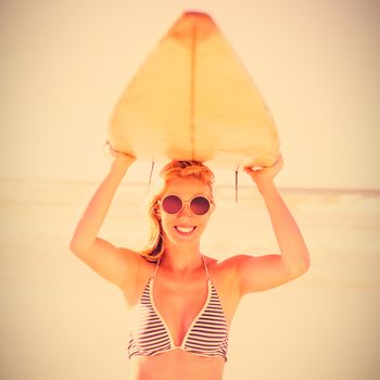 Portrait of young woman carrying surfboard at beach during sunny day