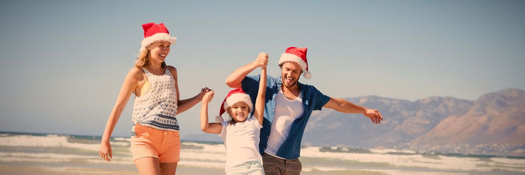 Happy family wearing Santa hat while enjoying at beach during sunny day