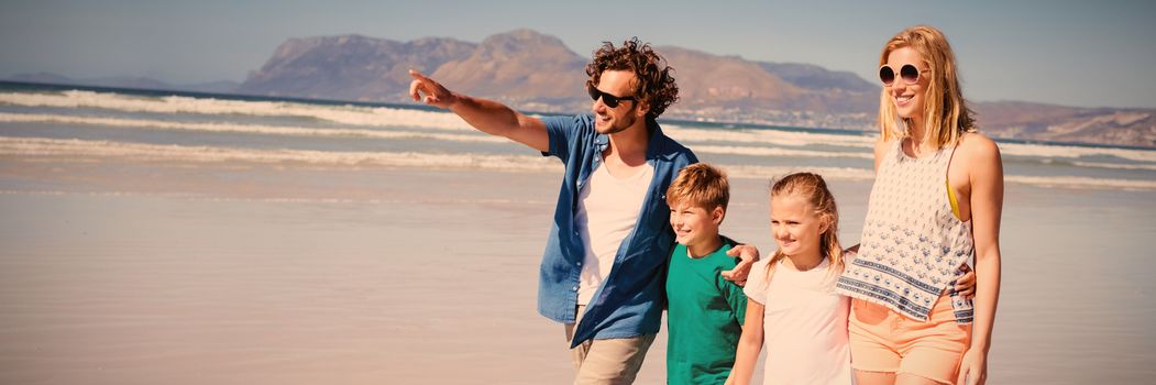 Happy man pointing away with family walking at beach during sunny day