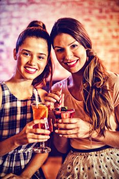 Portrait of two young women having cocktail drinks in pub