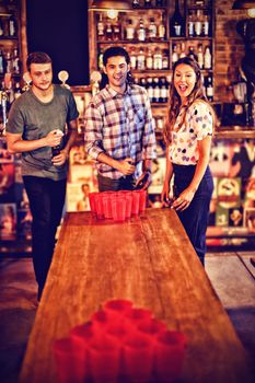 Group of happy friends playing beer pong game in pub