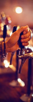 Close-up of bartender hands using beer tap in pub