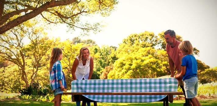 Family spreading the tablecloth on picnic table in park