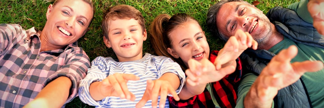 Happy family lying on the grass and making hand gestures in the park