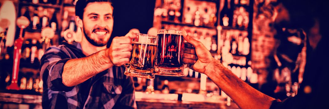 Two young men toasting their beer mugs in pub