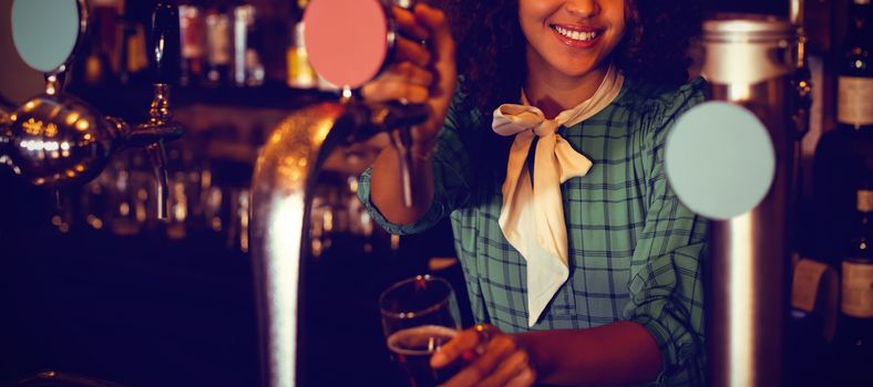 Portrait of waitress using beer tap at counter in pub