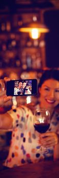 Young women taking a selfie from mobile phone while having a red wine in pub