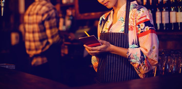 Waitress taking an order on notepad at counter in pub