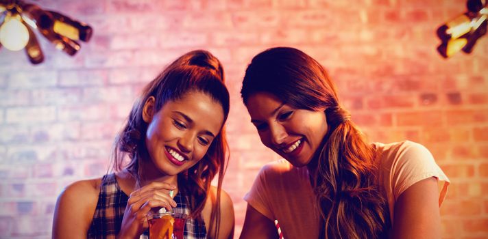 Two young women using mobile phone in pub
