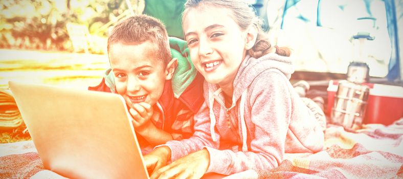 Smiling siblings using laptop outside the tent at campsite