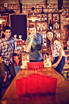 Group of happy friends playing beer pong game in pub