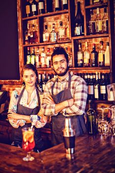 Portrait of waiter and waitress standing with arms crossed at counter in pub