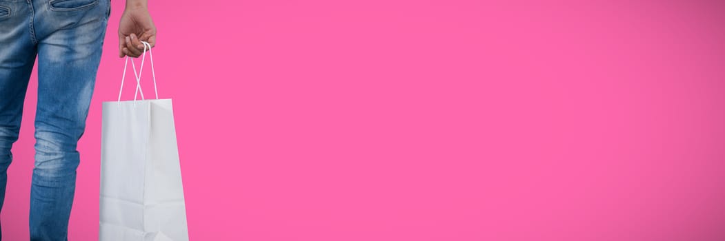 Mid section of man carrying shopping bag against pink background