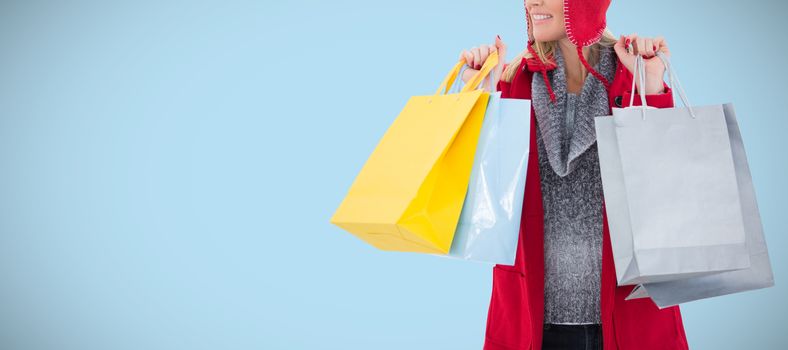 Blonde in winter clothes holding shopping bags against blue background