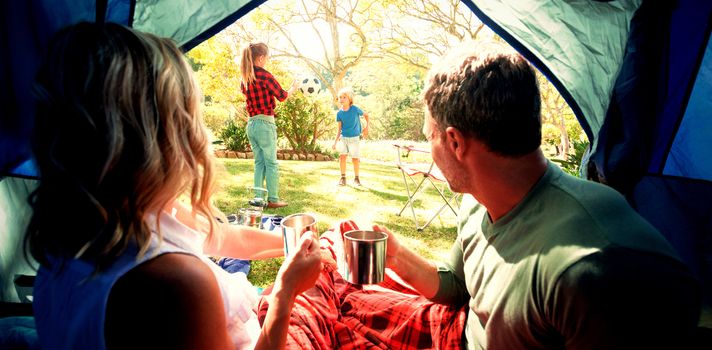 Rear view of couple having coffee and looking at kids playing outside the tent