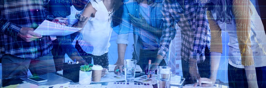 Smiling business people working at table against stocks and shares