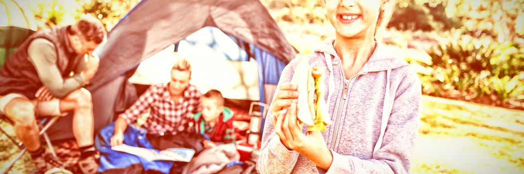 Portrait of smiling girl holding a sandwich while family sitting outside the tent