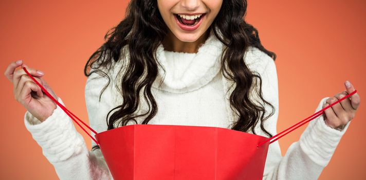 Happy woman with christmas hat opening red shopping bag against abstract yellow background