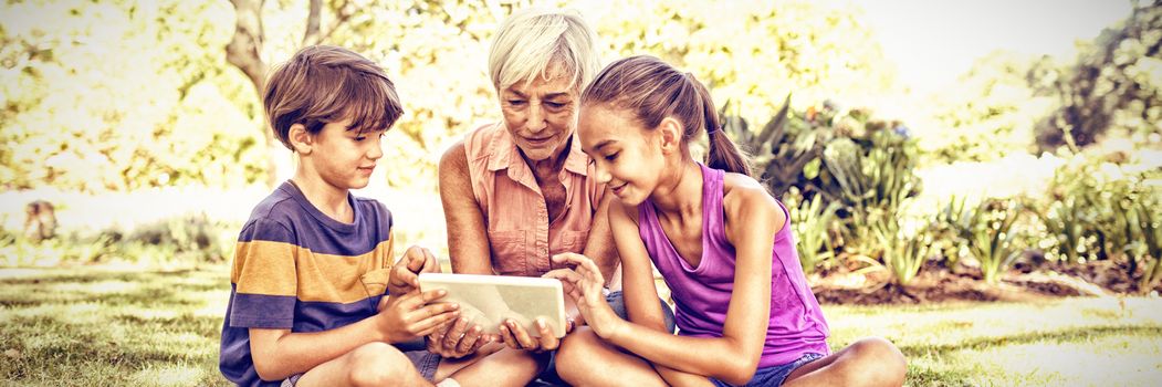 Grandmother and grand kids using digital tablet in the park on sunny day