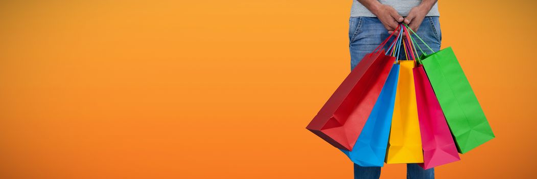 Low section of man carrying colorful shopping bag standing against white background against abstract saffron background