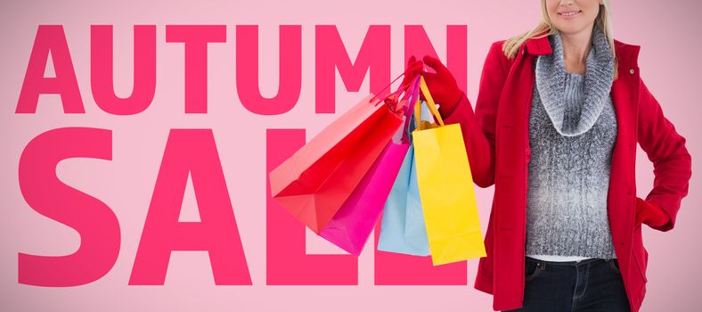 Blonde in winter clothes holding shopping bags against pink background