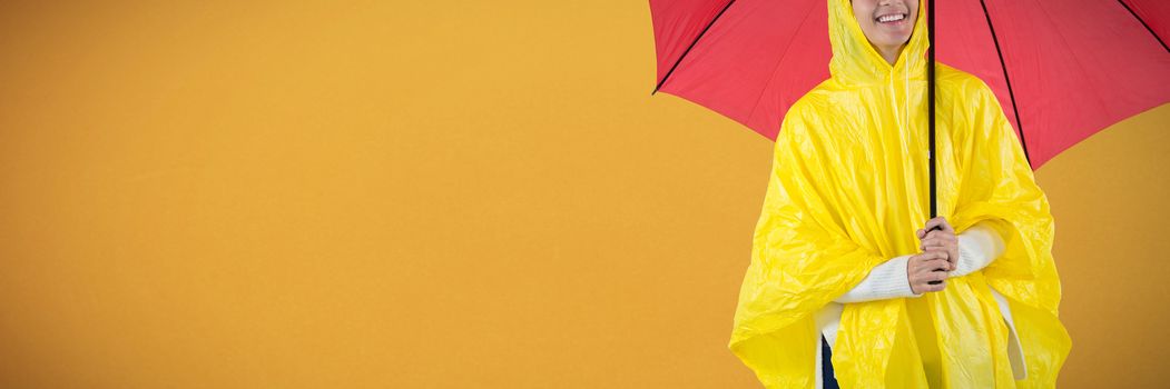 Woman in yellow raincoat holding an umbrella against orange background