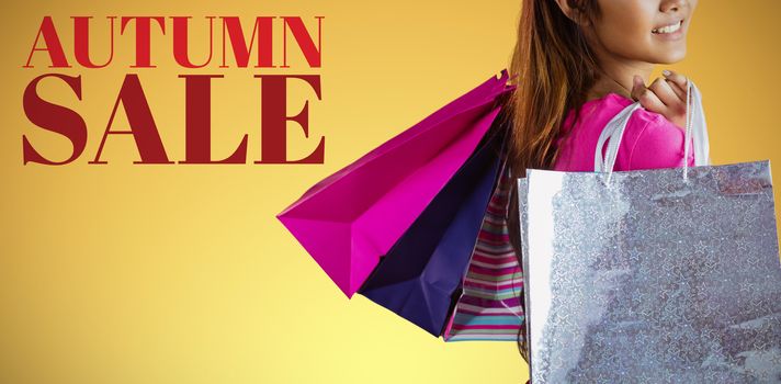 Smiling asian woman with shopping bags against abstract yellow background