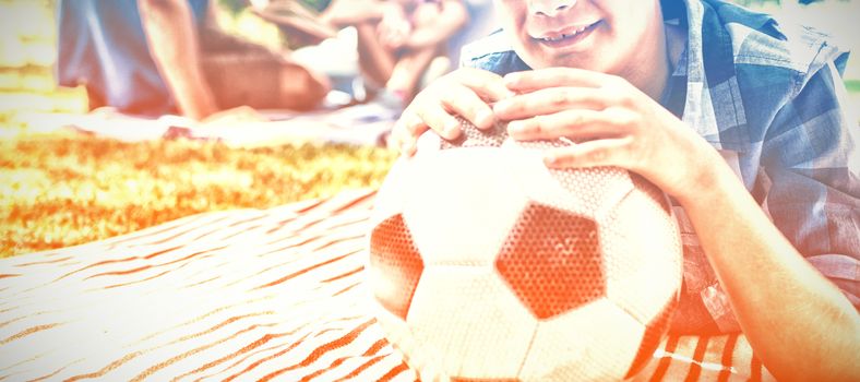 Portrait of smiling boy leaning on his football in picnic at park on a sunny day