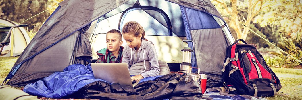 Kids using laptop in the tent at campsite