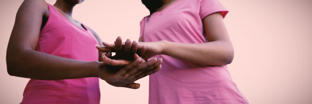 two black women joining hands against pink background 