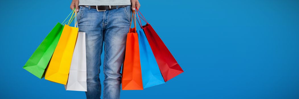 Low section of man carrying colorful shopping bag against abstract blue background