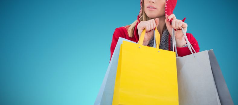 Blonde in winter clothes holding shopping bags against abstract blue background