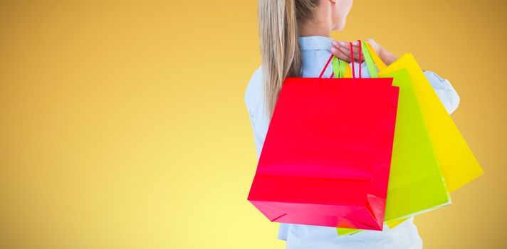 Pretty blonde holding shopping bags against abstract yellow background
