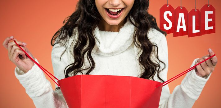 Happy woman with christmas hat opening red shopping bag against abstract yellow background