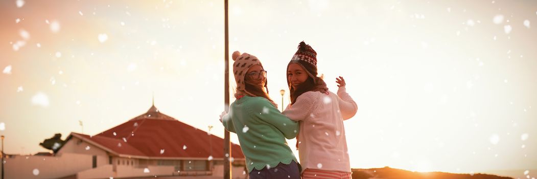 Snow falling against female friends walking on wall during sunset