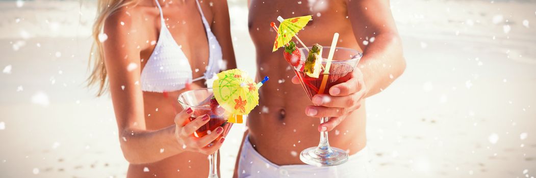 Snow falling against attractive young couple smiling at camera holding cocktails