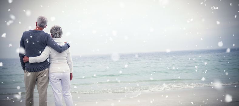 Snow falling against rear view of senior couple embracing at beach