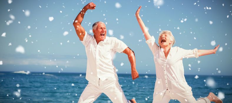 Snow falling against senior couple jumping at the beach