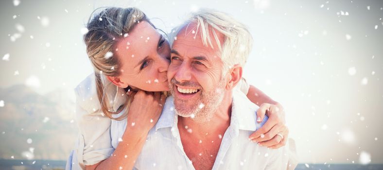 Man giving his smiling wife a piggy back at the beach against snow falling