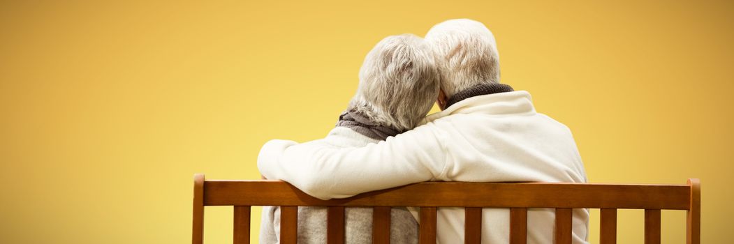  Senior couple embracing on a bench against abstract yellow background