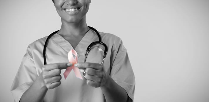Smiling nurse holding breast cancer awareness pink ribbon with both hands on a pink background