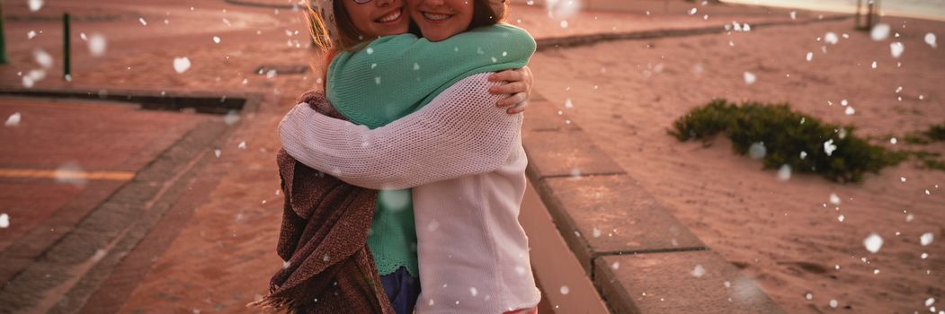 Snow falling against female friends hugging each other