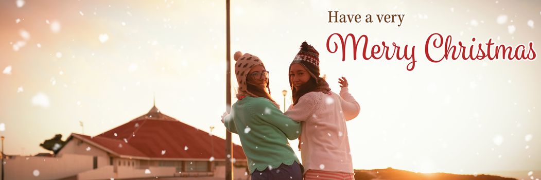 Christmas card against female friends walking on wall during sunset